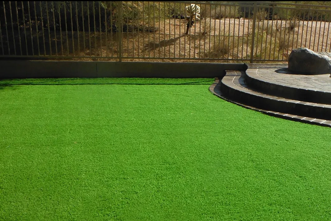 Bright green artificial lawn in a desert backyard with paver steps and an iron fence