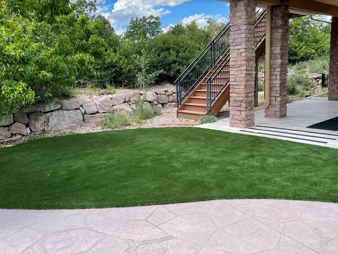 Artificial turf backyard curving between a stone retaining wall and a stamped concrete patio